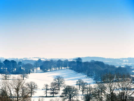 Countryside landscape across rural setting with Winter snow on ground and bright blue sky backgroundの写真素材