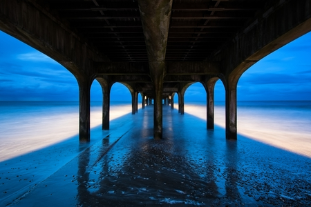 Twilight landscape of pier stretching out into sea with moonlightの写真素材