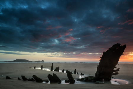 Dramatic sunset landscape over shipwreck on Rhosilli Bay beachの写真素材