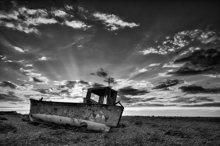 Abandoned fishing boat on shingle beach black and white landscape at sunsetの写真素材