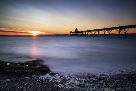 Stunning long exposure sunset over ocean with pier silhouette