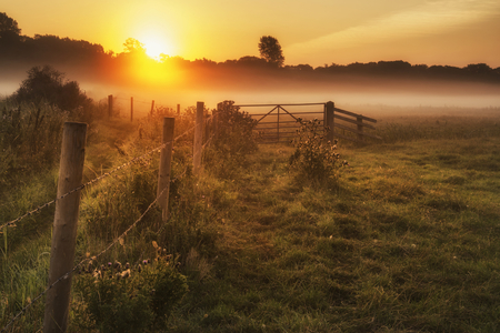 Beautiful sunrise landscape over foggy English countryside with glowing sunの写真素材