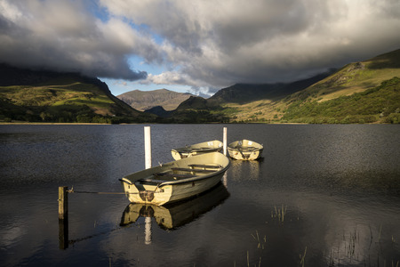 Beautiful moody stormy sky formations over stunning mountains lake landscape with rowing boats in foregroundの写真素材