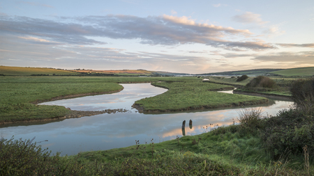 Beautiful sunrise landscape over English countryside with river slowly flowing through fieldsの写真素材