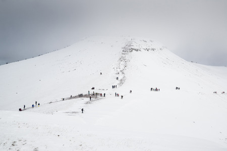Cloud covered winter landscape of Corn Du mountain in Brecon Beacons with hikersの写真素材