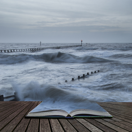 Beautiful moody stormy landscape image of waves crashing onto beach at sunrise in pages of bookの写真素材