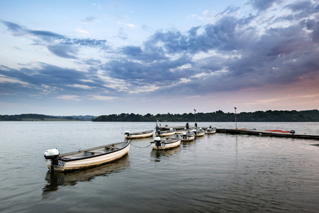 Summer sunset landscape image over calm lake with leisure boats on jettyの写真素材