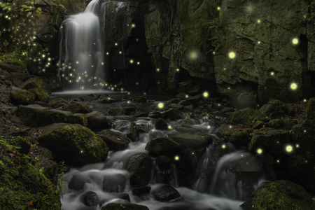 Beautiful ethereal fantasy image of fireflies over stream in rocky canyon landscape at duskの写真素材