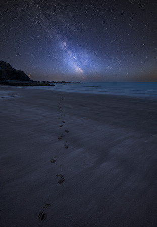 Stunning vibrant Milky Way composite image over landscape of Footprints on empty beach Summer...