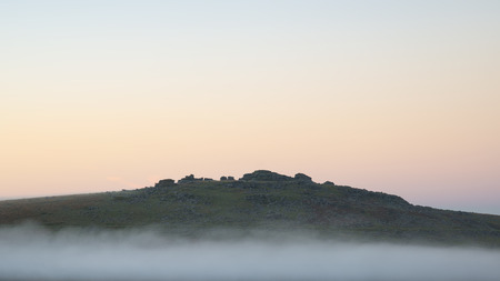 Stunning foggy sunrise landscape over the tors in Dartmoor revealing peaks through the mistの写真素材