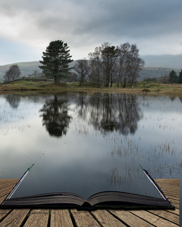 Beautiful landscape image of moody storm clouds over Kelly Hall Tarn in Lake District during late Autumn Fall afternoon coming out of pages of open story bookの写真素材