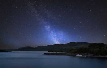 Stunning vibrant Milky Way composite image over landscape of calm lake with boat on shoreの写真素材