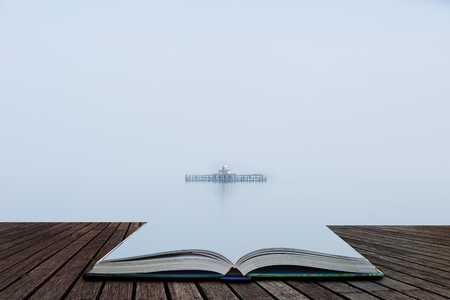 Fine art minimalist landscape image of derelict pier remains at sea during foggy morning giving appearance of ruins floating coming out of pages of open story bookの写真素材