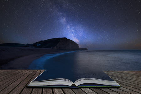 Stunning vibrant Milky Way composite image over landscape of long exposure of West Bay in Dorset  coming out of pages in magical story bookの写真素材