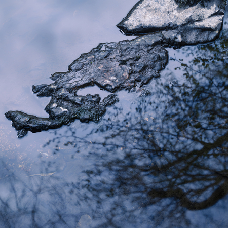 Abstract landscape image of trees reflected in river with rock providing contrastの写真素材