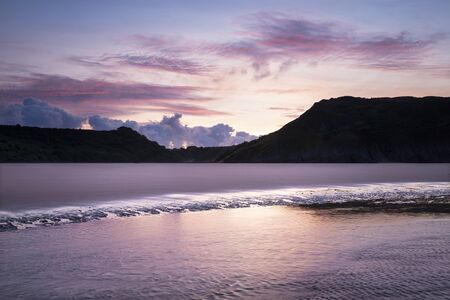 Stunning colorful Summer sunrise landscape image of Three Cliffs Bay in South Walesの写真素材