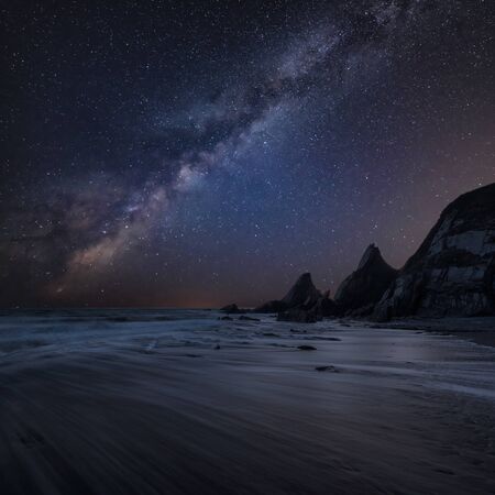 Beautiful composite landscape image of Mily Way core over sea rocks and cliffs with long exposure tide on beachの写真素材