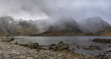 Stunning dramatic Winter landscape image of Llyn Idwal and snowcapped Glyders Mountain Range in Snowdoniaの写真素材