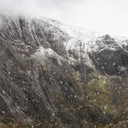 Stunning dramatic landscape image of snowcapped Glyders mountain range in Snowdonia during Winter with menacing low clouds hanging at the mountain peaksの写真素材