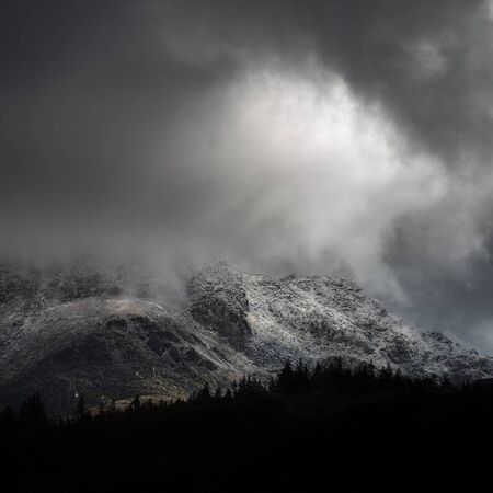 Stunning moody dramatic Winter landscape image of snowcapped Tryfan mountain in Snowdonia during...
