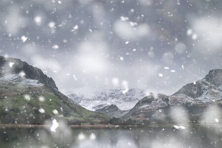 Beautiful sunrise landscape image in Winter of Llyn Nantlle in Snowdonia National Park with snow capped mountains in background in heavy snow stormの写真素材