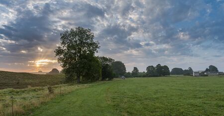 Beautiful Summer sunrise landscape image over English countryside with mist hanging in fields