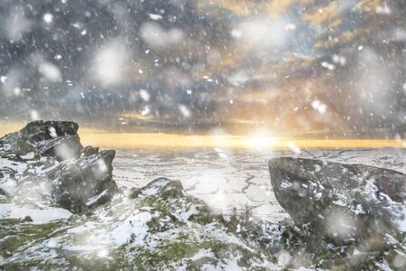 Stunning Winter sunset landscape from mountains looking over countryside in heavy snow storm
