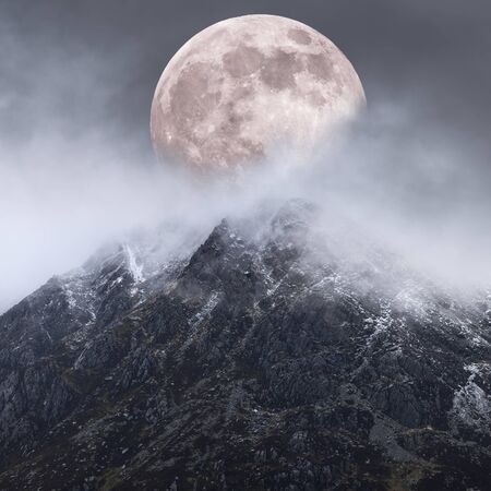Beautiful digital composite image of Supermoon above mountain range giving very surreal fantasy look to the dramatic landscape imageの写真素材