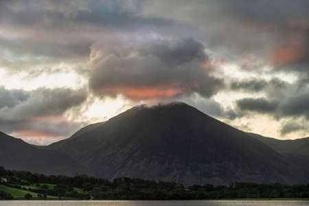 Stunning sunrise landscape image looking across Loweswater in the Lake District towards Low Fell and Grasmere with colorful sky breaking on the mountain peaksの写真素材