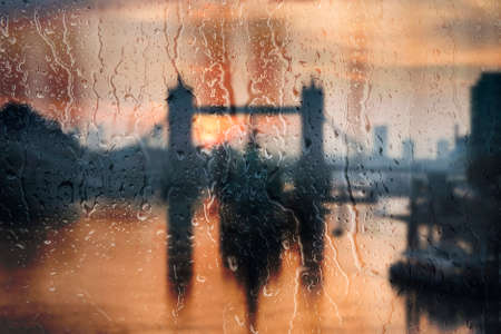Beautiful landscape conceptual view of London City through glass window with raindrops running down...