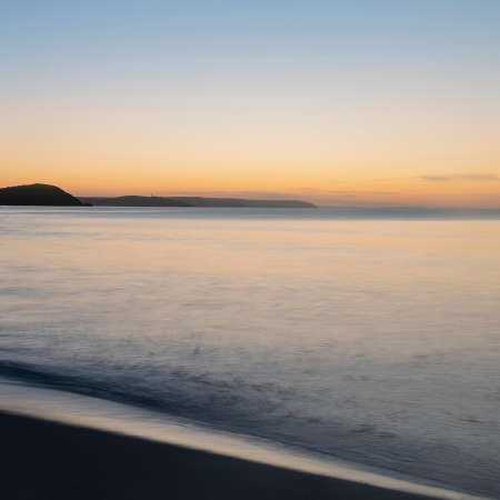 Stunning sunrise over Pentewan Sands in Cornwall with vibrant sky and long exposure oceanの写真素材