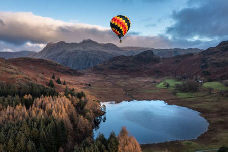 Digital composite image of hot air balloons over Epic landscape image of sunrise from Blea Tarn in Lake Districtの写真素材