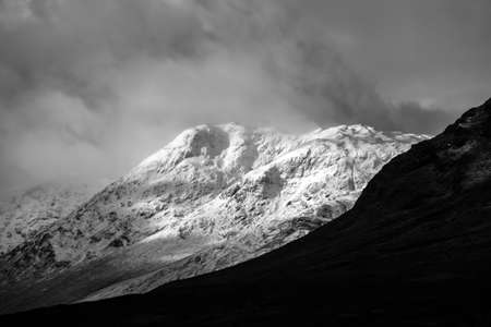 Black and white Stunning beautiful Winter landscape image of Lost Valley in Scotland with snowcapped Buachaile Etive Baeg sand distant mountain range with dramatic skyの写真素材