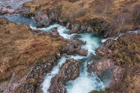 Beautiful aerial drone landscape image of vibrant River Coe flowing beneath snowcapped mountains in Scottish Highlandsの写真素材
