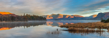 Epic Autumn sunrise landscape image looking from Manesty Park in Lake Distict towards sunlit Skiddaw Range with mit rolling across Derwentwater surfaceの写真素材