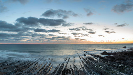 Stunning sunset landscape image of Welcome Mouth Beach in Devon England with beautiful rock...