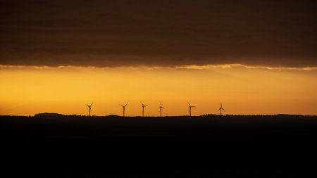 Moody landscape sunrise image of wind turbines against deep orange skyの写真素材