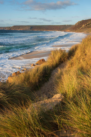 Beautiful landscape of Sennen Cove in Cornwall during sunset viewed from grassy sand dunes with moody sky and long exposure sea motionの写真素材