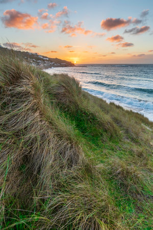 Beautiful landscape of Sennen Cove in Cornwall during sunset viewed from grassy sand dunes with moody sky and long exposure sea motionの写真素材