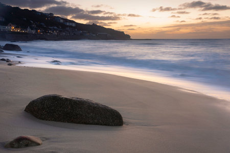 Beautiful landscape of Sennen Cove in Cornwall during sunset with moody sky and long exposure sea motionの写真素材