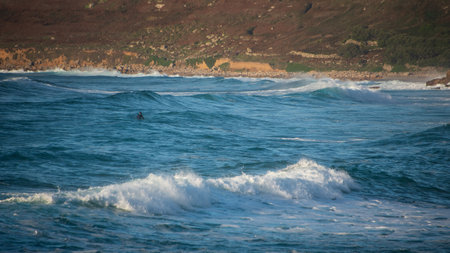 Unidentified surfers riding the waves at Sennen Cove in Cornwall during late sunsetの写真素材