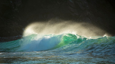 Epic landscape image of jade turquoise waves crashing onto shore and rocks in Kynance Cove Cornwall with glowing sunrise background and water spray droplets in windの写真素材
