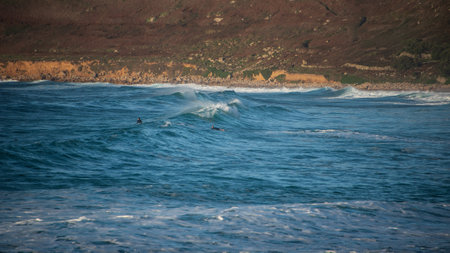 Unidentified surfers riding the waves at Sennen Cove in Cornwall during late sunsetの写真素材