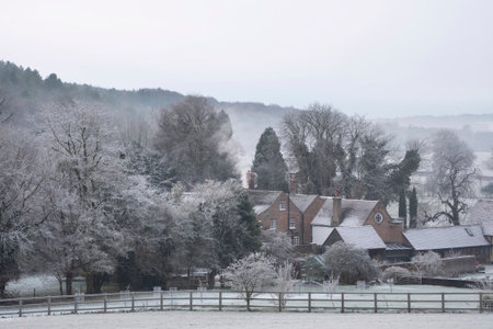 Beautiful Wintry landscape of farm in fog in English countryside at dawn with hoarfrost covering trees and buildingsの写真素材