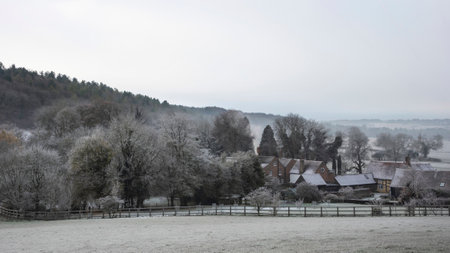 Beautiful Wintry landscape of farm in fog in English countryside at dawn with hoarfrost covering trees and buildingsの写真素材