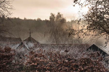Beautiful Wintry landscape of farm in fog in English countryside at dawn with hoarfrost covering trees and buildingsの写真素材