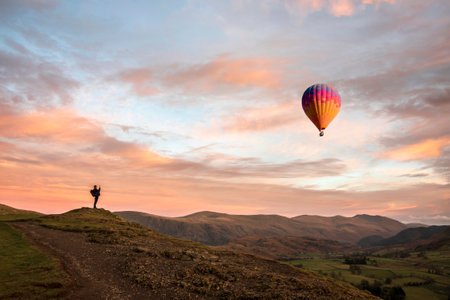 Wonderful sunset landscape image of view from Latrigg Fell towards Great Dodd and Stybarrow Dodd in Lake District with man photographing hot air ballon in landscapeの写真素材
