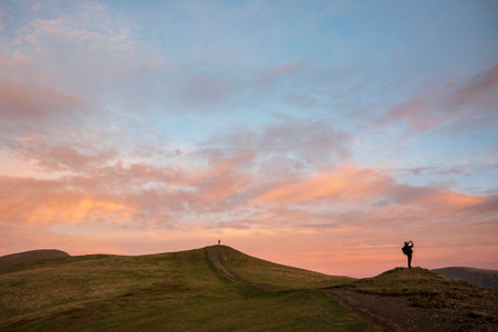 Beautiful Winter sunset landscape over Latrigg Fell in Lake District with two people on hilltop admiring sunsetの写真素材