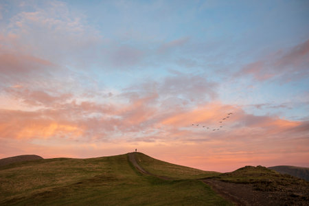 Beautiful Winter sunset landscape over Latrigg Fell in Lake District with single perosn on hilltop admiring sunsetの写真素材
