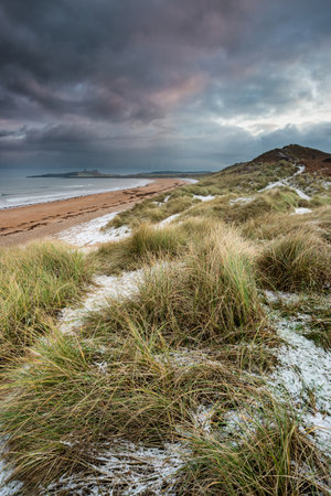 Beautiful unusual moody Winter landscape of snow on Embleton Bay beach in Northumberland Englandの写真素材